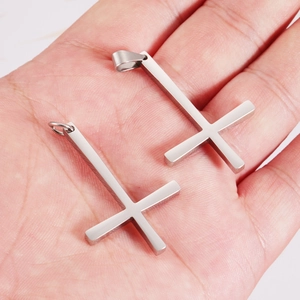 Polished stainless steel upside down cross pendant set held in palm for size reference
