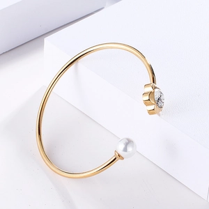 Detail of gold open bangle featuring a white pearl and sparkling crystal flower accent