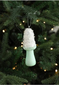 Glittery mint green and white mushroom ornament hanging on a Christmas tree with bokeh light