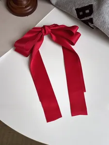 Barrette nœud en satin rouge avec longs rubans sur un fond esthétique minimaliste