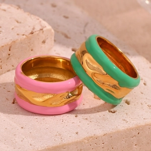 Detail of pink and green enamel rings with gold wavy metal bands on stone background