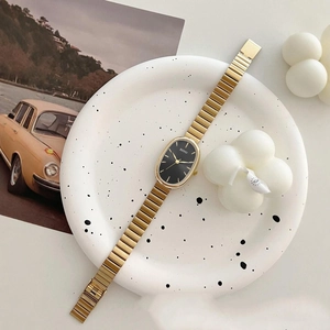 Elegant gold metal strap watch with oval black dial and minimalist markers on artistic plate