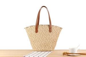 Detailed view of a woven straw tote bag with brown leather handles on a wooden table