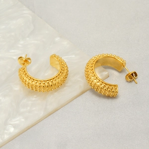 Detailed close-up of C-shaped gold-plated stud earrings with beaded metal texture