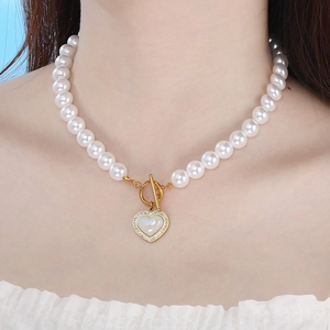 Close-up of pearl necklace featuring a gold heart pendant with shell inlay and diamonds