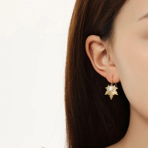 Detailed close-up of a gold starburst drop earring with a pearl center on a model
