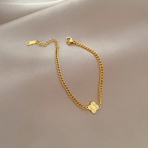Close-up of golden stainless steel clover chain bracelet on silk fabric background