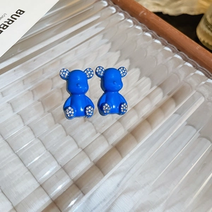 Macro shot of blue flocked bear earrings with rhinestone details on textured glass