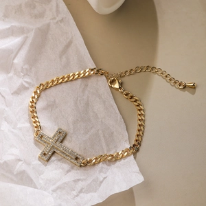 Detail of gold-plated cross bracelet with cubic zirconia on textured background