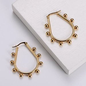 Detailed close-up of golden teardrop earrings with decorative small beads on white base