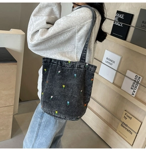 Détail de la broderie florale colorée sur un grand sac cabas en denim noir délavé