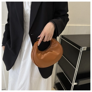 Detail of a brown leather crescent bag with gold zipper and smooth texture being held