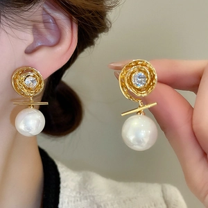Détail du clou doré à texture spirale avec zircon et une grande perle blanche pendante