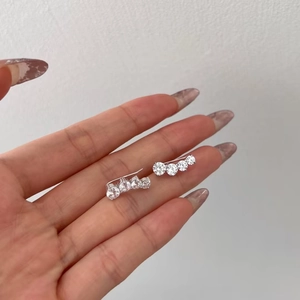 Close-up of small silver S925 earrings with four clear zircons shown on a finger for size