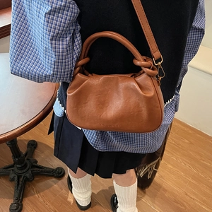 Brown leather crossbody bag with knot handle and chain strap in daily life setting