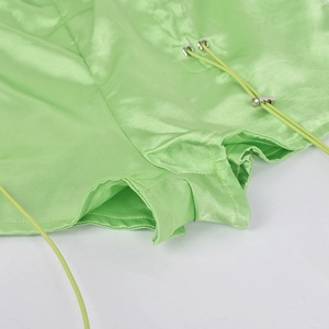 Detail of neon green satin shorts with drawstring and metal eyelets on white background