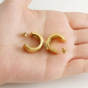 Gros plan de boucles d'oreilles en C dorées 18K avec zircon placées dans la main