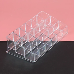 Close-up of tiered acrylic lipstick organizer with grid slots on a pink and black background