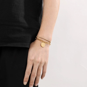 Detailed view of a gold double-layer stainless steel bracelet with a round pendant on a model