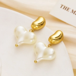 Detailed shot of gold bean studs with pearl heart dangles on a white display stand