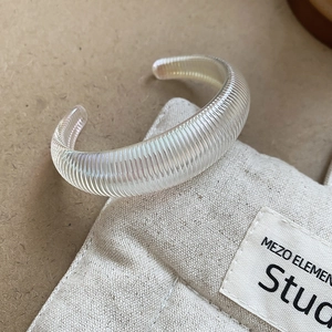 Macro detail of a translucent ribbed open bangle on a beige linen studio background