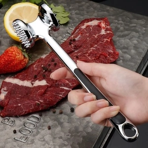 Close-up of a meat tenderizer with ergonomic black handle over raw meat on a steel board