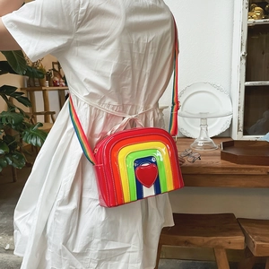 Rainbow striped crossbody bag with red heart detail and colorful fabric strap shown on model