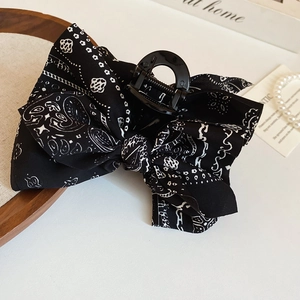 Détail macro d'une pince à cheveux avec nœud en tissu noir à motifs paisley et textures chics