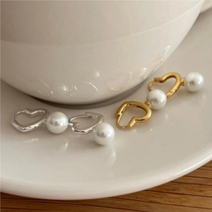 Detail view of heart-shaped pearl earrings in gold and silver on a white ceramic saucer