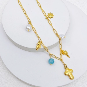 Golden ocean necklace with cross, seahorse charms and baroque pearls on stone stand