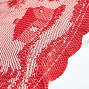 Detailed close-up of red Christmas lace tablecloth with festive house and snowflake patterns