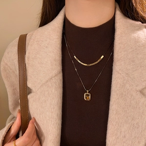 Close-up of double-layer gold necklace featuring amber gemstone pendant on a female model
