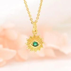 Close-up of gold evil eye necklace with green gemstone and zircon sunflower pendant