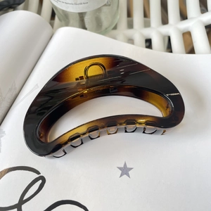 Close-up of amber resin hair claw clip with curved teeth on a white book aesthetic