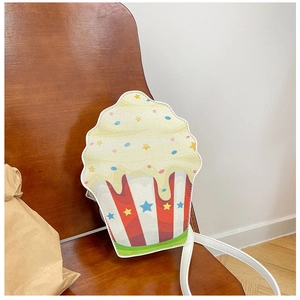 Detail view of a glittery cupcake crossbody bag on a wooden chair with white leather strap