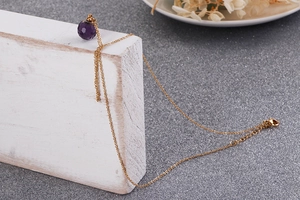 Detail of a purple faceted crystal pendant on a gold titanium steel necklace with lobster clasp