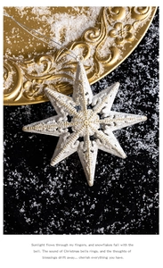 White and gold octagonal star ornament with glitter on a snowy black backdrop