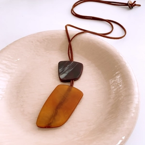 Detail of irregular resin pendant on a cord necklace displayed in a ceramic dish