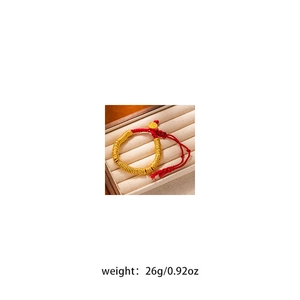 Detail of red rope bracelet with gold beads and god of wealth pendant on beige velvet box