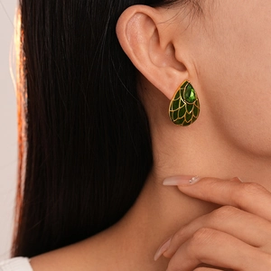 Gros plan de boucles d'oreilles goutte émail vert avec écailles d'or et gemme sur l'oreille