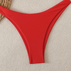 Close-up of vibrant red V-cut high-waisted bikini bottoms on a summer beach texture