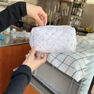 Detailed shot of a quilted white makeup bag featuring red cherries and beige zipper