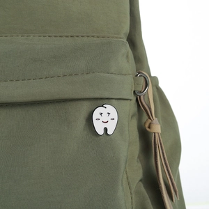 Detailed view of a cute cartoon tooth enamel pin attached to a green canvas backpack