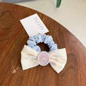 Detailed view of light blue floral scrunchie with pearl bow on a wooden surface