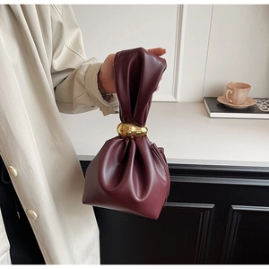 Detail of burgundy ruched cloud bag with large golden metal rings on the handle