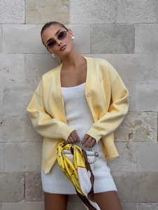 Detail of light yellow knit cardigan paired with a white textured mini dress and bag