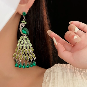 Gros plan sur des boucles d'oreilles paon avec des strass verts et des cristaux brillants