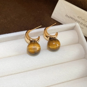 Macro shot of gold half-moon earrings with brown tiger eye beads in a white jewelry box