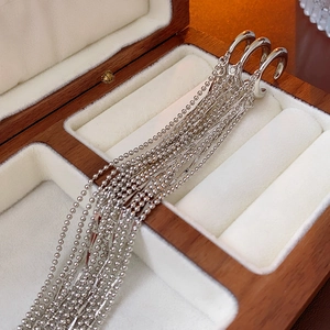 Detailed view of silver tassel ear cuffs with long bead chains on a wood jewelry box