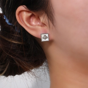 Close-up of a silver square stud earring with white inlay and a bee motif on ear